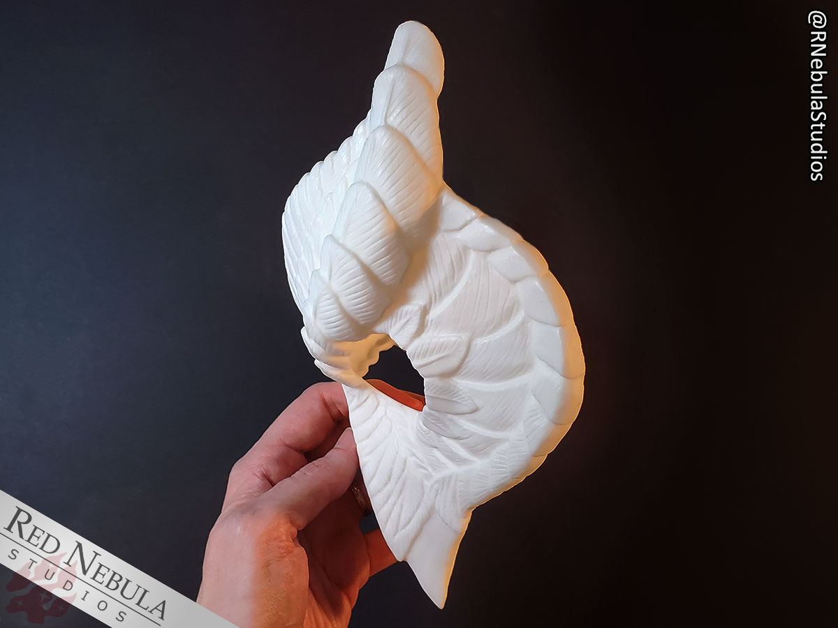 The blank white resin owl mask, shown from the side with the beak of the mask pointed straight down.